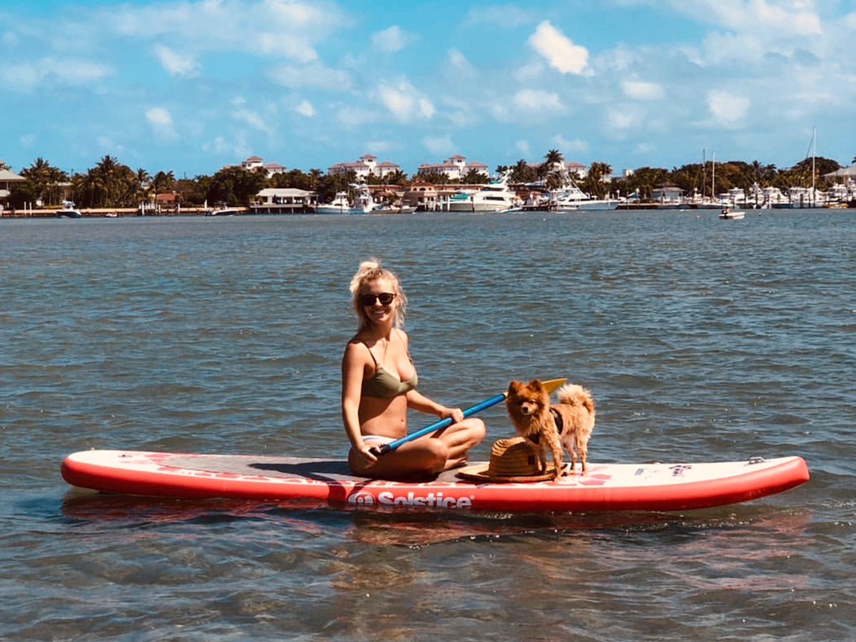 Girl and her dogs sitting on a Solstice Watersports Inflatable SUP Paddle Board in the water.