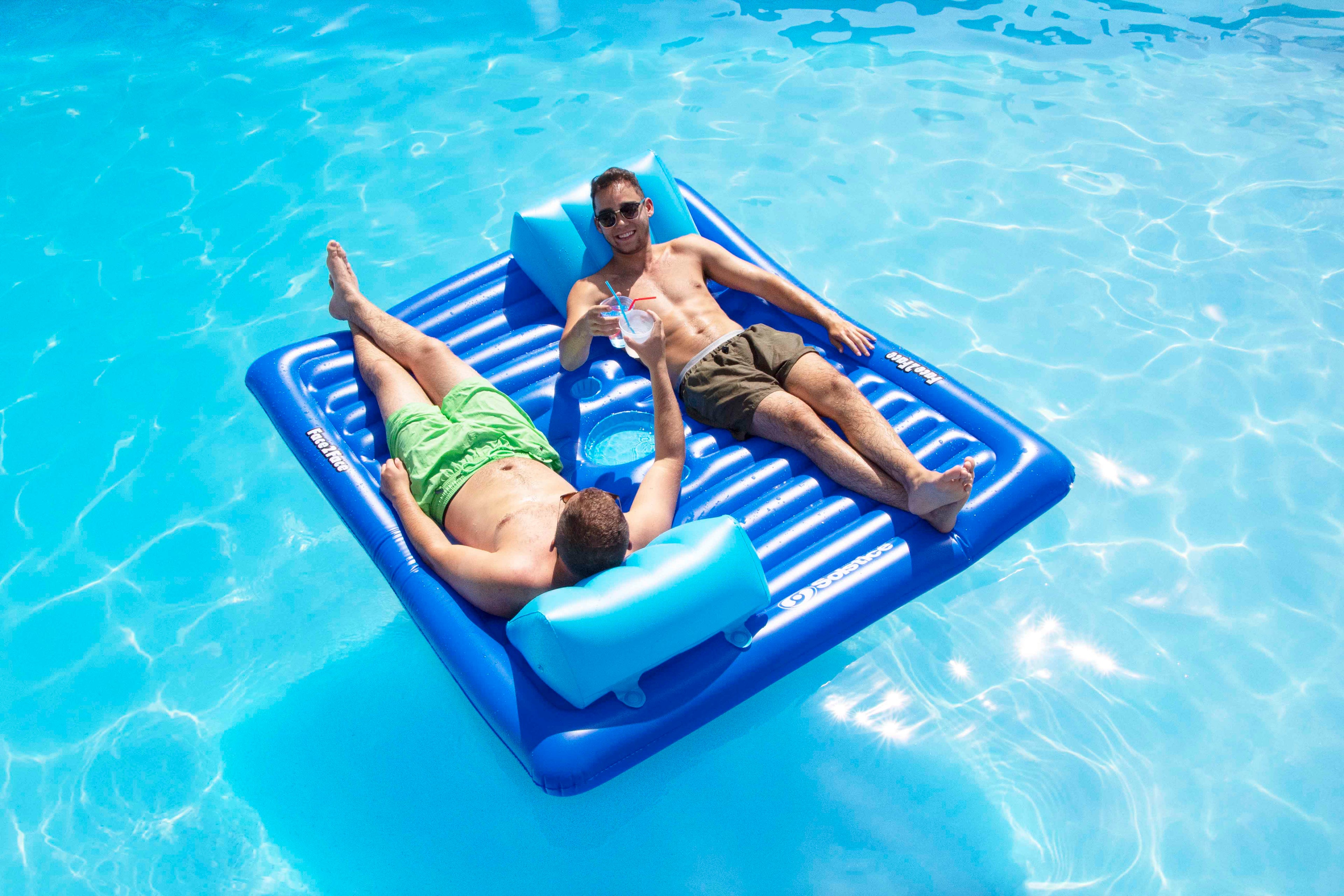 Two people lying on a blue inflatable raft in a pool.