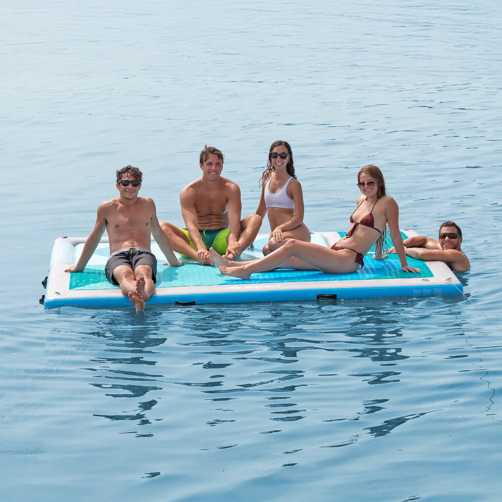 Group of five people sitting on a Solstice Convertible Slide Dock in flat dock mode on a calm lake