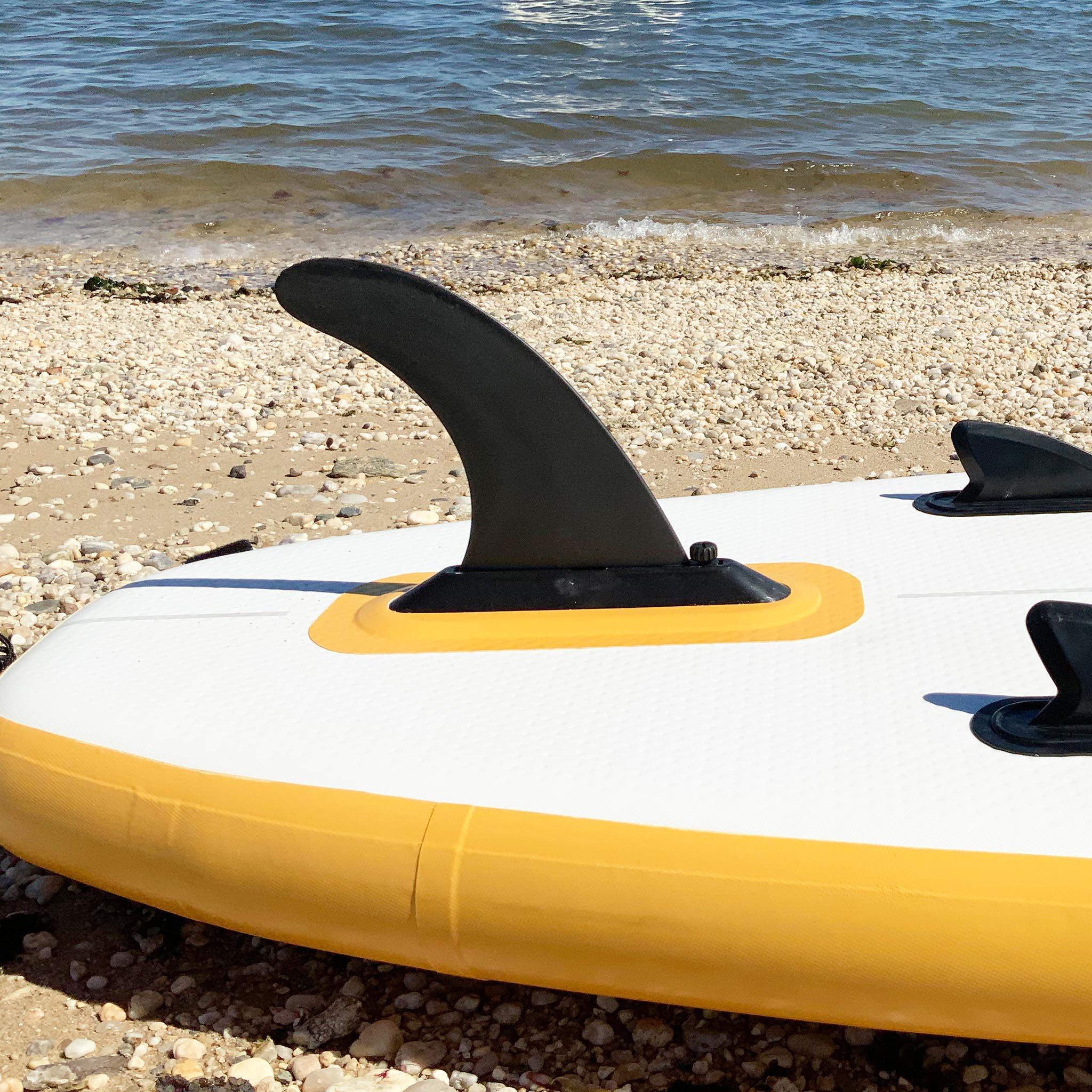 Inflatable white and yellow paddle board with black fins on sandy beach near water